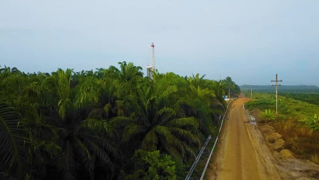 Cinematic Drone Shot of Onshore Drilling and Workover Rig structure and Rig equipment for oil exploration and exploitation in the middle of jungle surrounded by palm oil trees during sunset time.