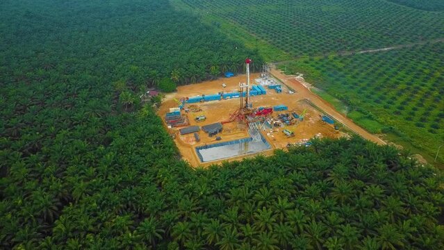 Cinematic Drone Shot of Onshore Drilling and Workover Rig structure and Rig equipment for oil exploration and exploitation in the middle of jungle surrounded by palm oil trees during sunset time.