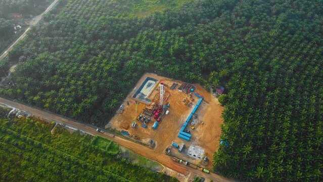Cinematic Drone Shot of Onshore Drilling and Workover Rig structure and Rig equipment for oil exploration and exploitation in the middle of jungle surrounded by palm oil trees during sunset time.