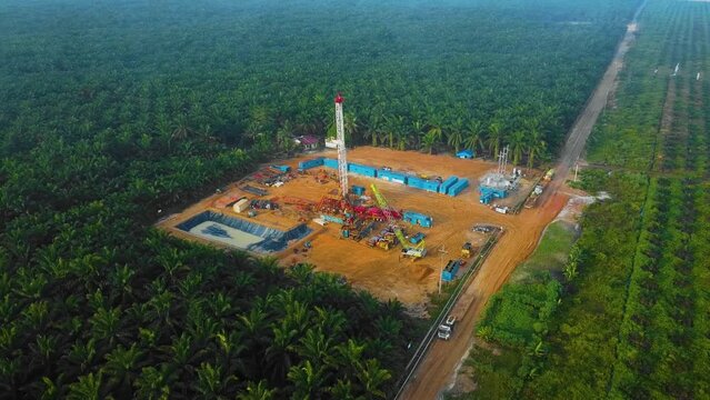 Cinematic Drone Shot of Onshore Drilling and Workover Rig structure and Rig equipment for oil exploration and exploitation in the middle of jungle surrounded by palm oil trees during sunset time.