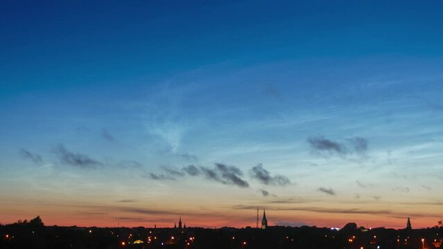 Beautiful time lapse of silvery (noctilucent, polar mesospheric) clouds glowing and shining in a summer evening, calm and tranquil scenic view after the sunset, cityscape, wide angle shot
