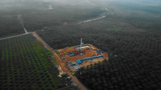 Cinematic Drone Shot of Onshore Drilling and Workover Rig structure and Rig equipment for oil exploration and exploitation in the middle of jungle surrounded by palm oil trees during sunset time.
