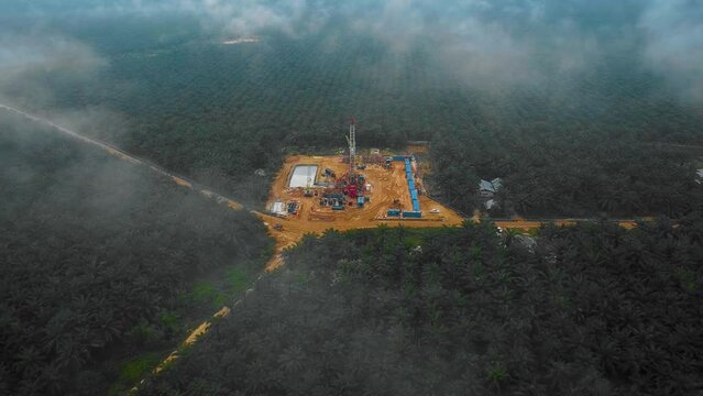 Cinematic Drone Shot of Onshore Drilling and Workover Rig structure and Rig equipment for oil exploration and exploitation in the middle of jungle surrounded by palm oil trees during sunset time.