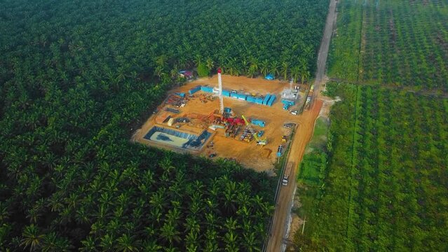 Cinematic Drone Shot of Onshore Drilling and Workover Rig structure and Rig equipment for oil exploration and exploitation in the middle of jungle surrounded by palm oil trees during sunset time.