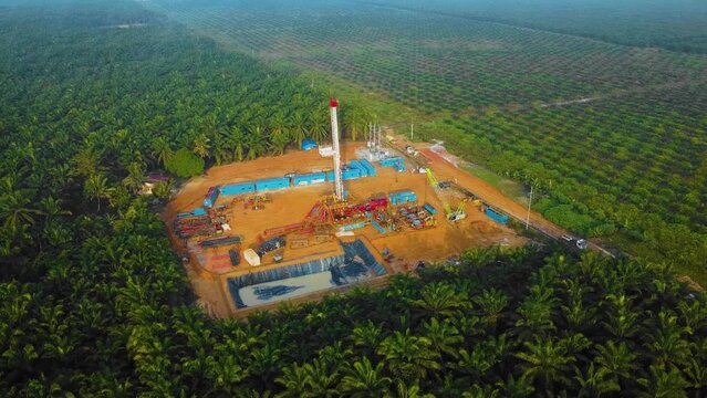 Cinematic Drone Shot of Onshore Drilling and Workover Rig structure and Rig equipment for oil exploration and exploitation in the middle of jungle surrounded by palm oil trees during sunset time.