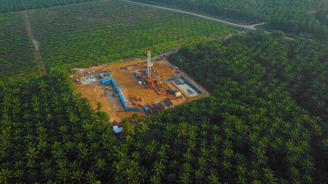 Cinematic Drone Shot of Onshore Drilling and Workover Rig structure and Rig equipment for oil exploration and exploitation in the middle of jungle surrounded by palm oil trees during sunset time.