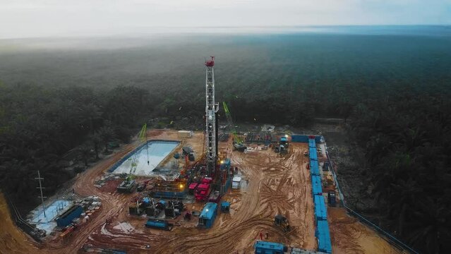 Cinematic Drone Shot of Onshore Drilling and Workover Rig structure and Rig equipment for oil exploration and exploitation in the middle of jungle surrounded by palm oil trees during sunset time.