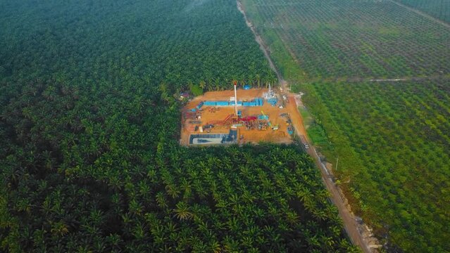 Cinematic Drone Shot of Onshore Drilling and Workover Rig structure and Rig equipment for oil exploration and exploitation in the middle of jungle surrounded by palm oil trees during sunset time.