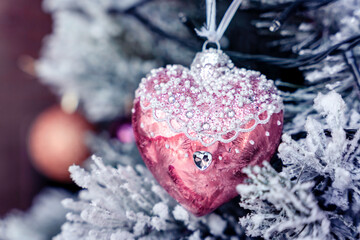 Pink heart Christmas decoration bauble with white glass beads on a snowy tree with a crystal