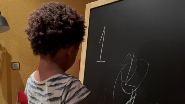 Lovely and exotic two year old afro american child doing his first drawings with a chalk in a board at home