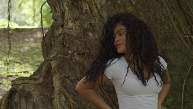 Close up of sexy young hispanic model playing in her hair standing in front of a large tree