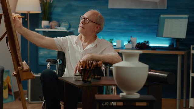 Senior man living with physical disability and drawing authentic vase model on canvas, art and craft hobby. Dealing with chronic impairment in wheelchair, draw professional masterpiece.