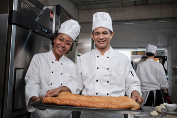 Portrait of professional chefs in white uniform looking at camera with a cheerful smile and proud with tray of bread in kitchen. A friend and partner of pastry foods and fresh daily bakery occupation.