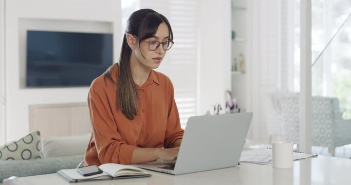 Businesswoman reading a report and writing in a notebook while checking a phone and working from home alone. One focused female business professional typing an email on a computer and browsing online