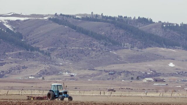 Farmer plowing field with tractor in the countryside of Wyoming in Star Valley during Spring.