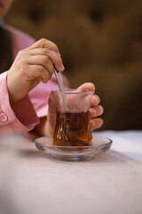 The girl is stirring black tea in a Turkish cup with a spoon.