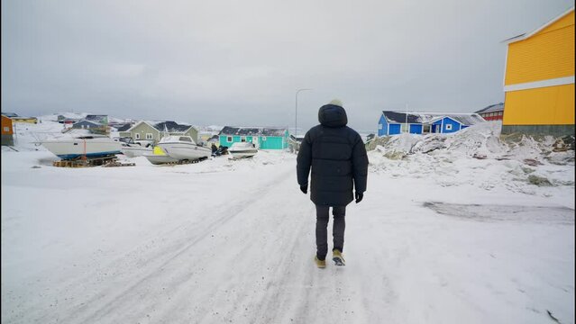 Man In Winter Coat Walking Through Snow Covered Street Of Ilulissat