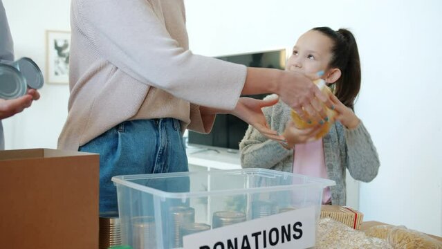 Kind child helping mother and father collecting food products for donation box indoors in apartment. Charity and humanitarian aid concept.