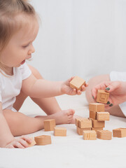 Fototapeta na wymiar Mom is playing with a child, building a house out of wooden eco-friendly cubes, close-up. The concept of early child development through games. Cozy homely atmosphere. Mother's Day, Child's Day