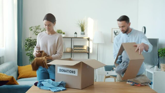 Man and woman packing clothes in donation box at home when child bringing teddy bear sharing toy. Family lifestyle and charity concept.