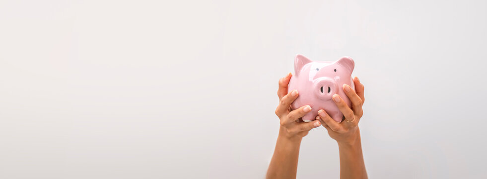 Hand of female holding pink piggy bank on gray backgrounds, saving money concept, image panorama for cover design.