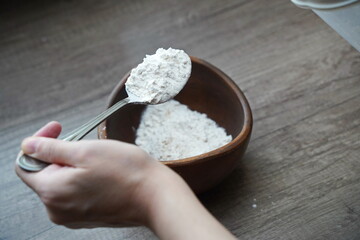 A woman holds a spoon with flour in her hands