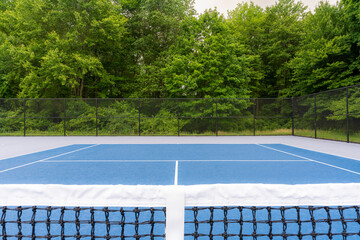 Tennis court net looking toward opponent, blue tennis court with white lines and gray out of bounds	