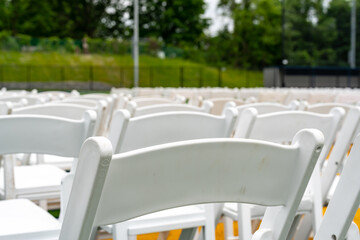 White chairs set-up in rows on a green synthetic turf athletic field for a high school graduation ceremony. 
