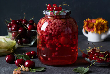 Homemade canned compote with sweet cherries and red currants in glass jar on gray background
