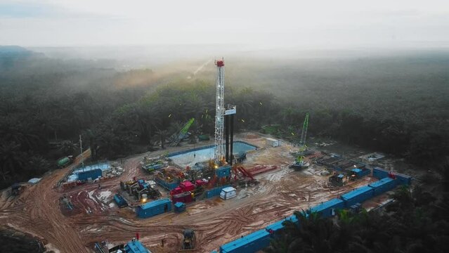 Cinematic Drone Shot of Onshore Drilling and Workover Rig structure and Rig equipment for oil exploration and exploitation in the middle of jungle surrounded by palm oil trees during sunset time.