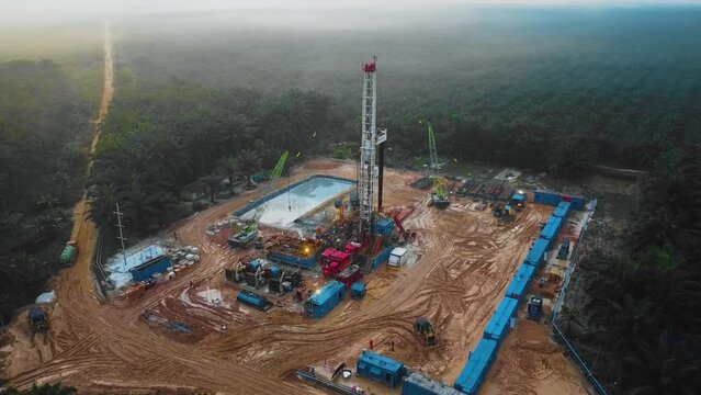 Cinematic Drone Shot of Onshore Drilling and Workover Rig structure and Rig equipment for oil exploration and exploitation in the middle of jungle surrounded by palm oil trees during sunset time.