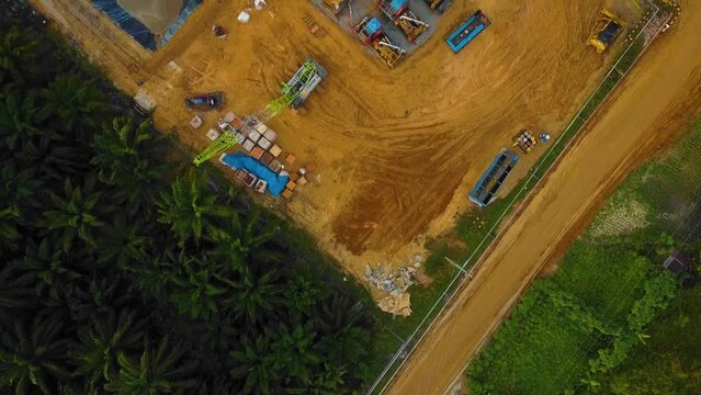 Cinematic Drone Shot of Onshore Drilling and Workover Rig structure and Rig equipment for oil exploration and exploitation in the middle of jungle surrounded by palm oil trees during sunset time.