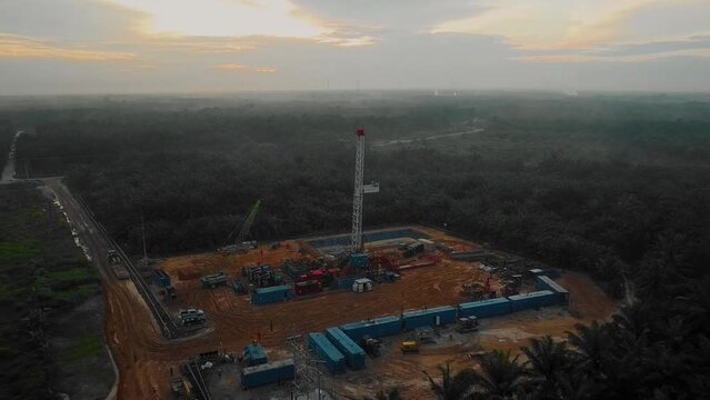 Cinematic Drone Shot of Onshore Drilling and Workover Rig structure and Rig equipment for oil exploration and exploitation in the middle of jungle surrounded by palm oil trees during sunset time.