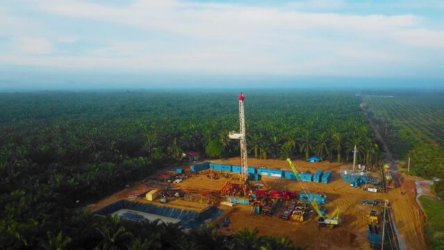 Cinematic Drone Shot of Onshore Drilling and Workover Rig structure and Rig equipment for oil exploration and exploitation in the middle of jungle surrounded by palm oil trees during sunset time.