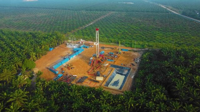 Cinematic Drone Shot of Onshore Drilling and Workover Rig structure and Rig equipment for oil exploration and exploitation in the middle of jungle surrounded by palm oil trees during sunset time.