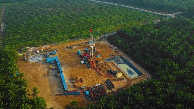Cinematic Drone Shot of Onshore Drilling and Workover Rig structure and Rig equipment for oil exploration and exploitation in the middle of jungle surrounded by palm oil trees during sunset time.
