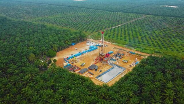 Cinematic Drone Shot of Onshore Drilling and Workover Rig structure and Rig equipment for oil exploration and exploitation in the middle of jungle surrounded by palm oil trees during sunset time.