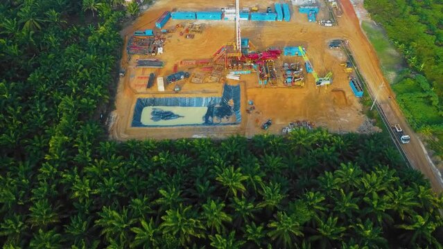 Cinematic Drone Shot of Onshore Drilling and Workover Rig structure and Rig equipment for oil exploration and exploitation in the middle of jungle surrounded by palm oil trees during sunset time.