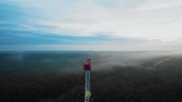 Cinematic Drone Shot of Onshore Drilling and Workover Rig structure and Rig equipment for oil exploration and exploitation in the middle of jungle surrounded by palm oil trees during sunset time.