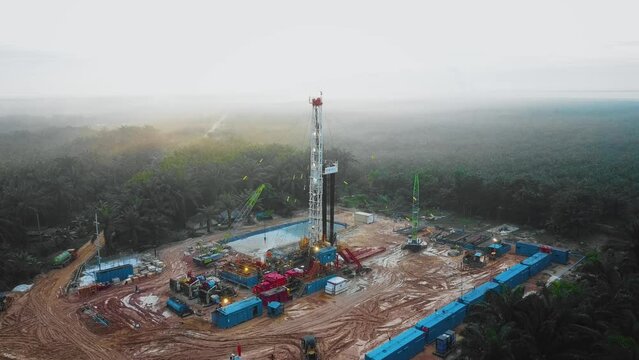 Cinematic Drone Shot of Onshore Drilling and Workover Rig structure and Rig equipment for oil exploration and exploitation in the middle of jungle surrounded by palm oil trees during sunset time.