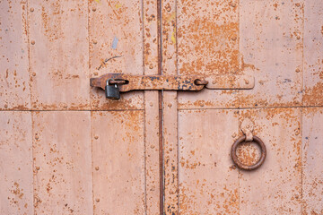The old iron gates are padlocked. Rivets and traces of rust on the metal surface are visible. Close-up. Background. Texture.
