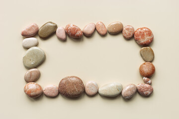 Aesthetic minimal frame of sea pebble stones on beige background with copy space. Square framing from natural smooth stone pastel pink, yellow colors. Summer concept, top view, empty space