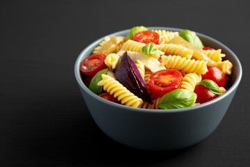 Homemade Fusilli Pasta Salad with Mozzarella and Vegetables in a Bowl on a black background, side view.