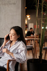 Attractive smiling young asian woman relaxing in cafe, working on laptop computer, talking on mobile phone
