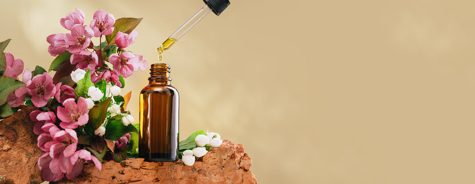Natural medicine or aroma oil or beauty essence concept vial with dropper on stone podium stand with pink flowers and golden brown background. Face and body spa serum care concept banner