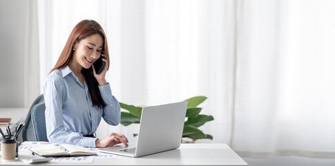 Elegant businesswoman using smartphone and working on laptop computer at office