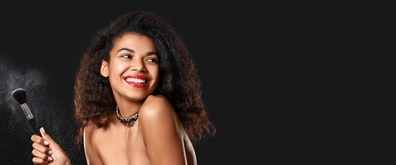 Portrait of beautiful African-American woman with makeup brush on dark background with space for...