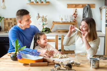 family cooks at home. mom, dad and daughter, knead the dough in a kitchen. man, girl, woman together