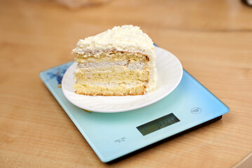 A piece of delicious cake with white butter cream lies on the scales. Calorie counting concept, figure tracking