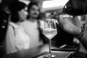 Shallow depth of field (selective focus) details with sparkling wine being poured into a glass at a bar.